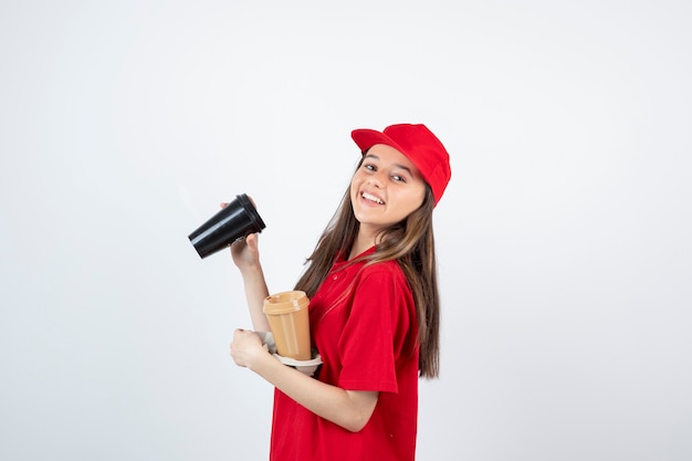 Jeune adolescente en uniforme rouge tenant deux tasses de café dans un carton