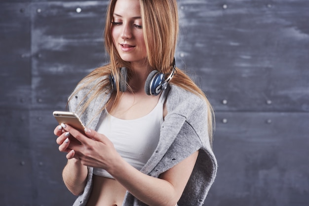 jeune adorable femme blonde avec un sourire craquant, portant un casque de monitoring professionnel noir sur fond gris studio