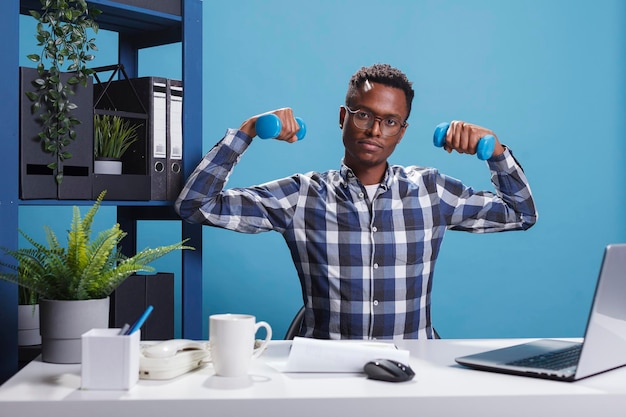 Photo jeune adulte actif et en bonne santé faisant de l'exercice avec des haltères de fitness afin de maintenir un corps fort. homme d'affaires athlétique de l'entreprise soulevant des poids assis au bureau au bureau.