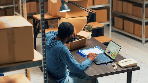 Jeune adulte analysant la chaîne d'approvisionnement et la logistique pour travailler sur la distribution, en utilisant la gestion des produits pour le développement des petites entreprises. Employé de bureau regardant le stock de rayonnages. Prise de vue à main levée.