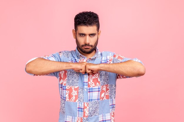 Jeune adulte barbu agressif debout gardant les poings ensemble, étant prêt à se battre, exprimant sa colère, ayant des émotions négatives. Tourné en studio intérieur isolé sur fond rose.