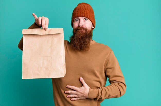 Jeune adulte barbu aux cheveux roux avec un sac en papier avec de la nourriture à emporter