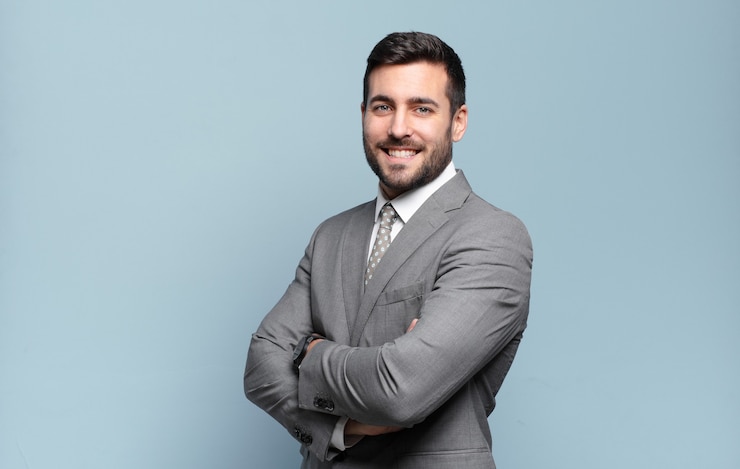 Photo jeune adulte bel homme d'affaires souriant à la caméra avec les bras croisés et une expression heureuse, confiante et satisfaite, vue latérale