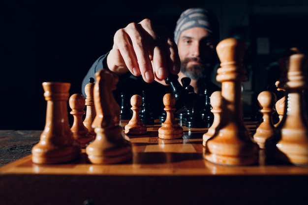 Jeune adulte bel homme jouant aux échecs dans l'obscurité avec côté allumé