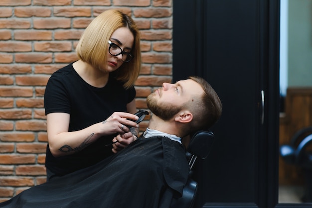 Jeune adulte belle femme caucasienne coiffeur coupe barbe bel homme au salon de coiffure moderne Heureux gay assis chaise hommes salon de beauté.
