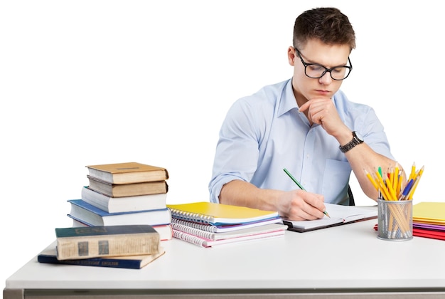 Un jeune adulte entouré de piles de livres et de cahiers écrit dans un cahier