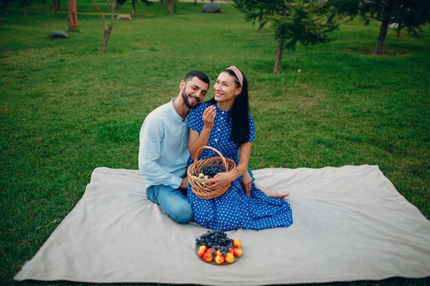 Jeune adulte femme et homme couple pique-nique assis au pré d'herbe verte dans le parc.