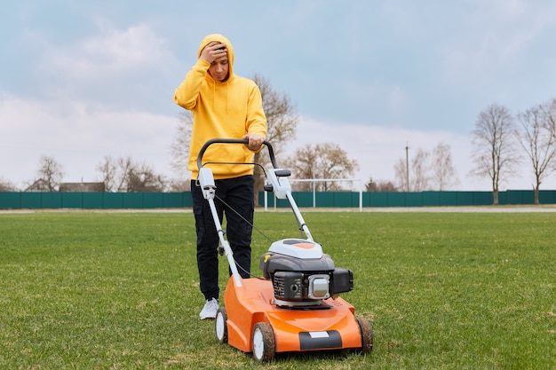 Jeune adulte jardinier attrayant tond la pelouse dans un grand champ