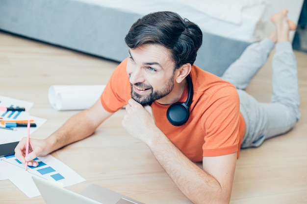 Jeune adulte positif souriant et regardant au loin tout en prenant des notes sur un nouveau projet