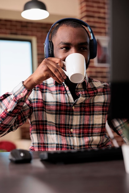 Jeune adulte travaillant à domicile sur ordinateur et écouter de la musique ou un podcast en ligne sur un casque. Homme utilisant un casque et naviguant sur le site Internet, faisant un travail indépendant à distance.