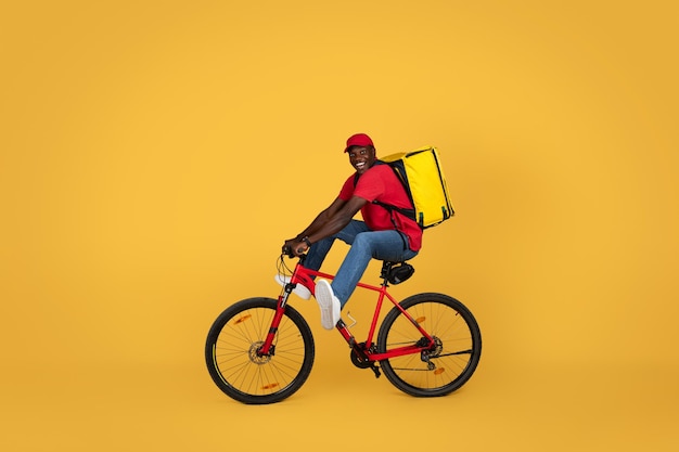 Photo un jeune afro-américain joyeux et excité, un livreur en uniforme avec un grand sac à dos, s'amuse à monter.