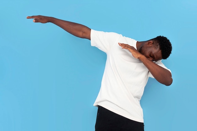 un jeune afro-américain en t-shirt blanc danse et fait du mouvement sur fond bleu