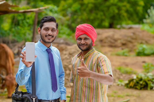 Jeune agent de banque ou agronome indien montrant un smartphone avec un agriculteur dans sa ferme