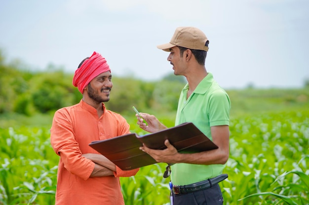 Jeune agent de banque indienne remplissant des papiers avec des agriculteurs dans un domaine agricole.