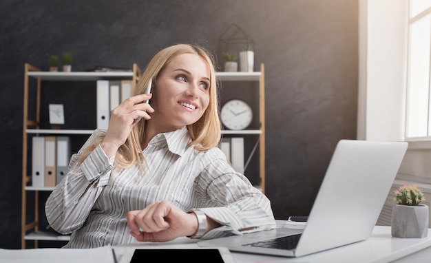 Jeune agent financier heureux ayant un appel d'affaires tout en travaillant sur un ordinateur portable au bureau