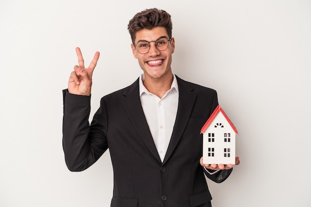 Jeune agent immobilier caucasien isolé sur fond blanc joyeux et insouciant montrant un symbole de paix avec les doigts.