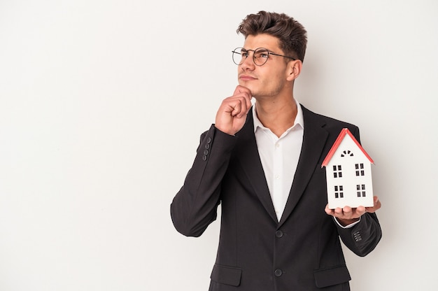 Jeune agent immobilier caucasien isolé sur fond blanc regardant de côté avec une expression douteuse et sceptique.