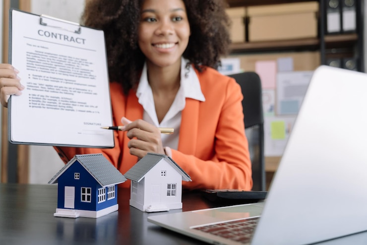 Photo un jeune agent immobilier travaille avec un ordinateur portable et une tablette à la table du bureau et une petite maison à côté.