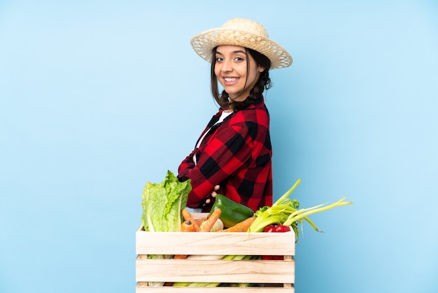 Jeune agriculteur femme tenant des légumes frais dans un panier en bois avec les bras croisés et impatient