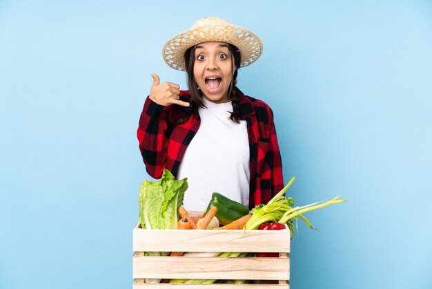 Jeune agriculteur femme tenant des légumes frais dans un panier en bois faisant le geste du téléphone. Rappelez-moi signe