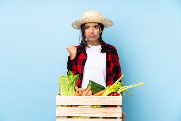 Jeune agriculteur femme tenant des légumes frais dans un panier en bois avec un geste de colère