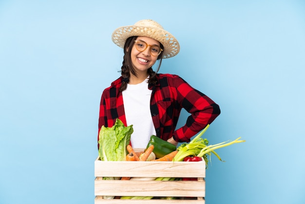 Jeune agriculteur femme tenant des légumes frais dans un panier en bois avec des lunettes et souriant