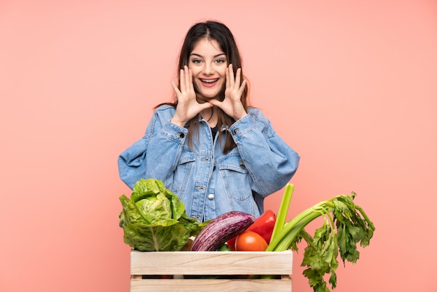 Jeune agriculteur femme tenant un panier plein de légumes frais criant avec la bouche grande ouverte