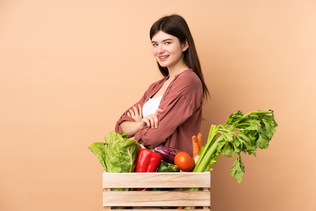 Jeune agriculteur fille avec des légumes fraîchement cueillis dans une boîte avec les bras croisés et impatient