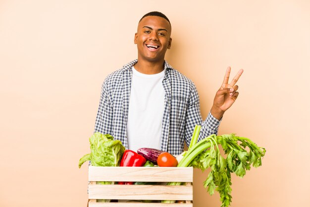 Jeune agriculteur homme sur un mur beige joyeux et insouciant montrant un symbole de paix avec les doigts.