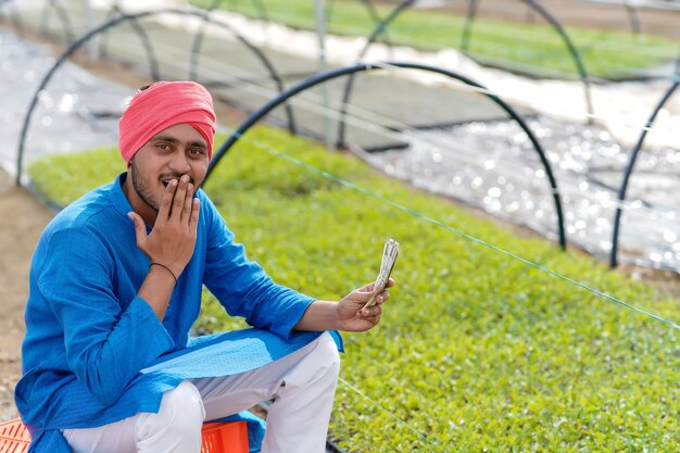 Jeune agriculteur indien comptant et montrant de l'argent à effet de serre