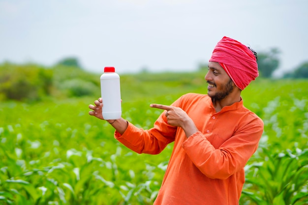 Jeune agriculteur indien montrant une bouteille d'engrais liquide sur le terrain agricole.