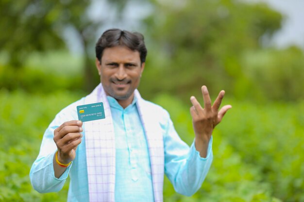 Jeune agriculteur indien montrant une carte de débit ou de crédit dans son champ d'agriculture verte