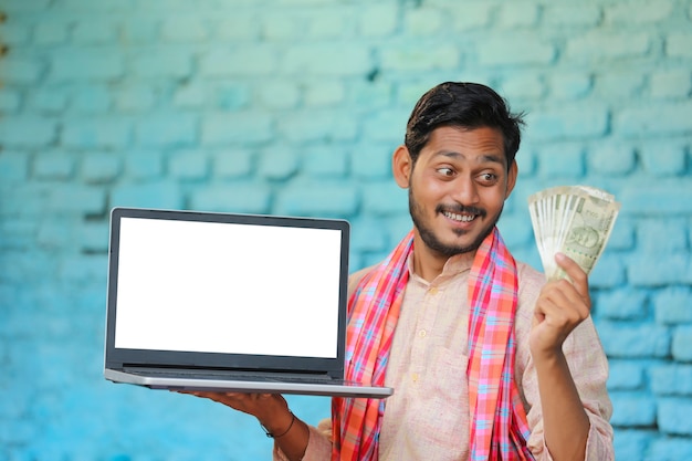 Jeune agriculteur indien montrant un écran d'ordinateur portable et de l'argent