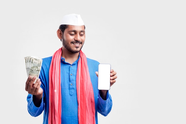 Jeune agriculteur indien montrant un smartphone et de l'argent sur fond blanc.