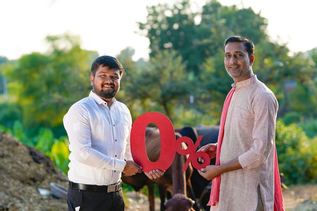 Jeune agriculteur indien montrant le symbole zéro pour cent avec un agronome ou un financier dans sa ferme