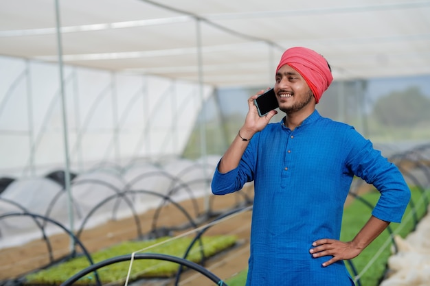 Jeune agriculteur indien parlant au téléphone intelligent à effet de serre
