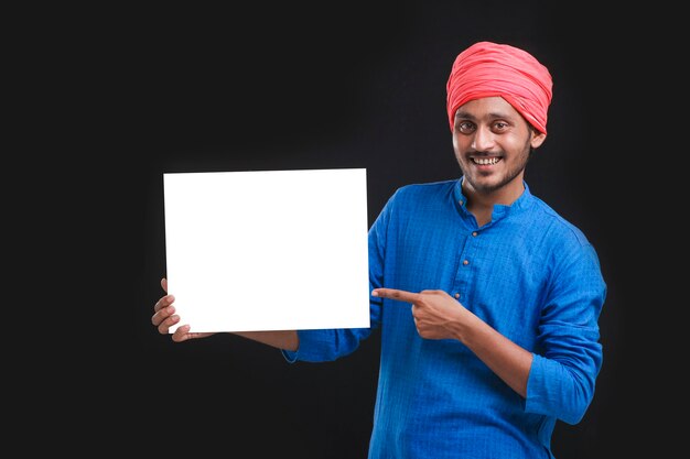 Jeune agriculteur indien tenant un carton blanc sur fond sombre.