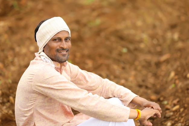 Jeune agriculteur indien en tenue traditionnelle et assis sur le terrain agricole.