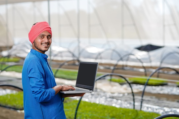 Jeune agriculteur indien utilisant un ordinateur portable à effet de serre ou maison poly