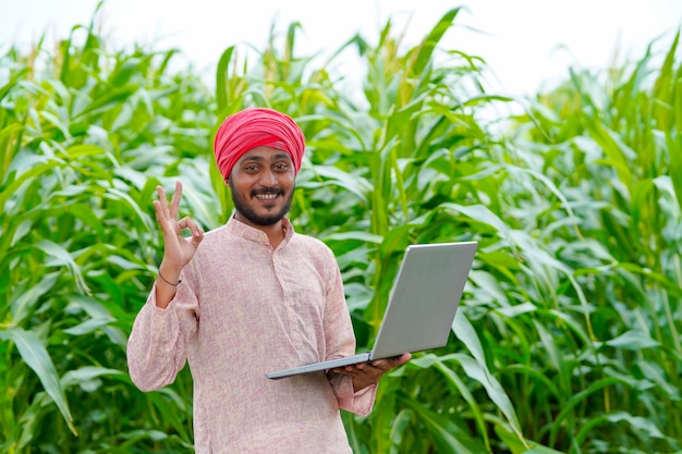 Jeune agriculteur indien utilisant un ordinateur portable sur le terrain agricole.