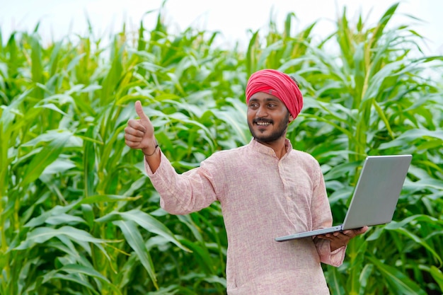 Jeune agriculteur indien utilisant un ordinateur portable sur le terrain agricole.