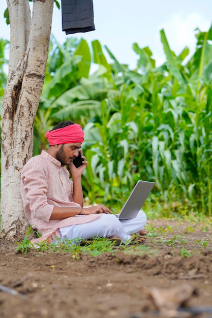 Jeune agriculteur indien utilisant un ordinateur portable sur le terrain agricole.