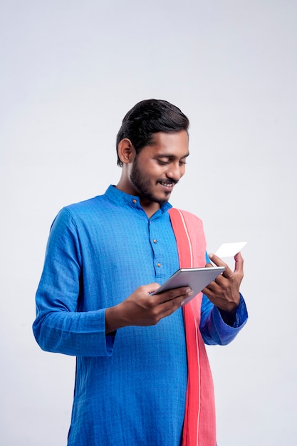 Jeune agriculteur indien utilisant un smartphone et une carte bancaire sur fond blanc.