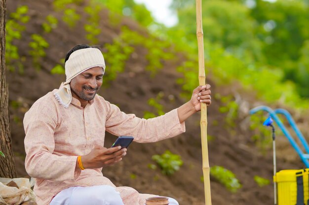 Jeune agriculteur indien utilisant un smartphone sur le terrain agricole.