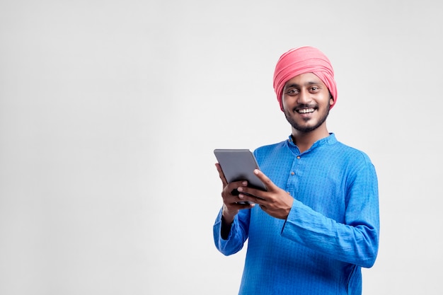 Jeune agriculteur indien utilisant une tablette et donnant une expression sur fond blanc.