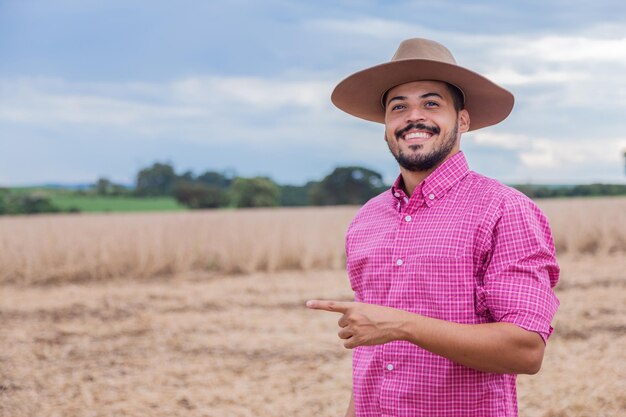 Jeune agriculteur latin travaillant sur un champ de blé pointant vers un espace libre pour le texte