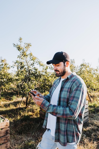 Jeune agriculteur latin utilisant son téléphone à côté d'une plantation de pommiers Concept agricole Nomade numérique