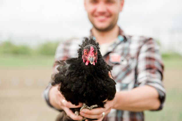 Un jeune agriculteur avec un poulet dans ses mains se tient dans son jardin dans le village.