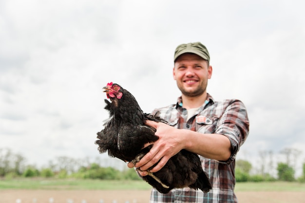 Un jeune agriculteur avec un poulet dans ses mains se tient dans son jardin dans le village.