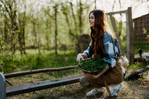 Une jeune agricultrice est assise devant une mangeoire à oiseaux et vérifie la composition du grain pour nourrir les poulets dans un enclos à la campagne